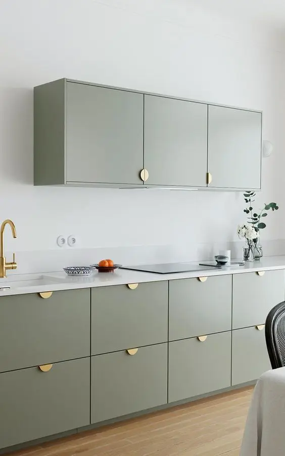 a modern and laconic kitchen with sage green cabinets, gold pulls, a white stone countertop and a small backsplash is chic