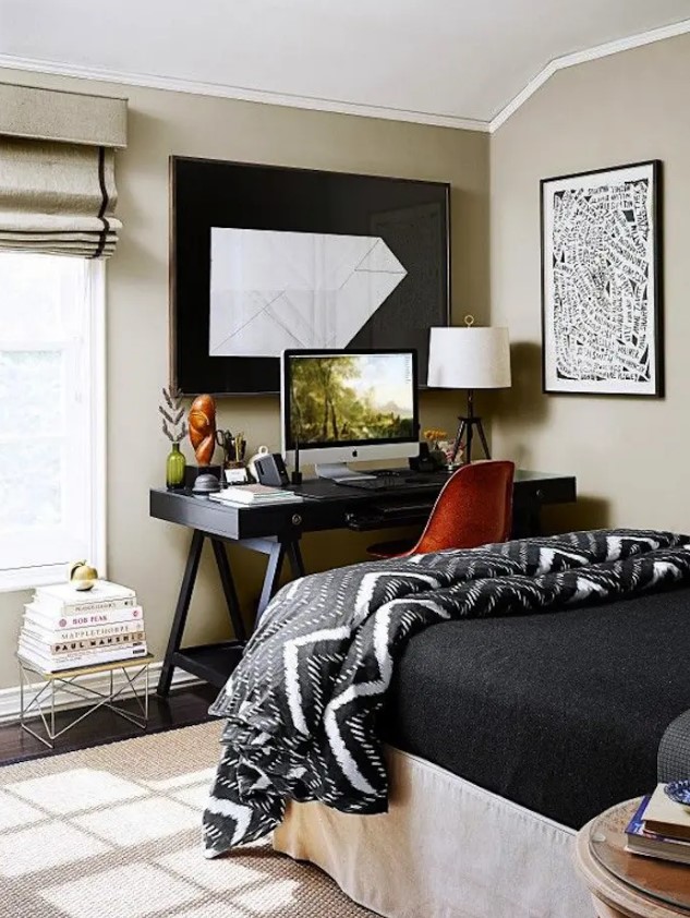a modern bedroom done in greige and black, with a bed with black bedding, a black trestle desk and a leather chair, some books and artwork