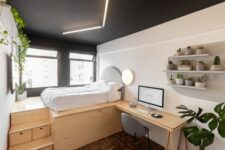 a modern bedroom with a black ceiling and lights, a built-in desk, a grey chair, open shelves and greenery