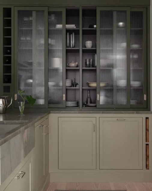 a modern classic greige kitchen with grey stone countertops and dark green fluted glass cabinets with sliding doors
