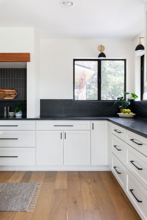 a modern famrhouse black and white kitchen with white shaker cabinets, black quartz countertops and a backsplash, black sconces