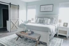 a modern farmhouse bedroom in pastel blue shades with white furniture, an upholstered bench, a vintage chandelier and ruffle bedding