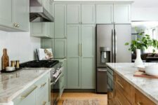 a modern sage green farmhouse kitchen with shaker cabients, a stained kitchen island, neutral stone countertops and gold fixtures
