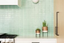 a modern white kitchen with a mint green small scale tile backsplash, black handles and cool planters on legs