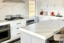 a modern white kitchen with shaker cabinets, a grey kitchen island, a white quratz backsplash and countertops plus a modern chandelier
