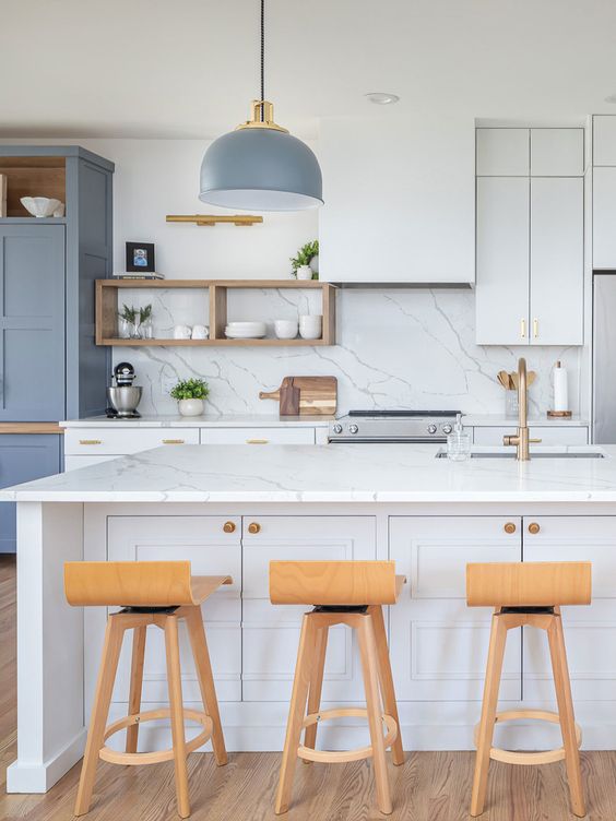 a modern white kitchen with shaker cabinets, white quartz countertops and a backsplash, a blue storage unit and a pendant lamp