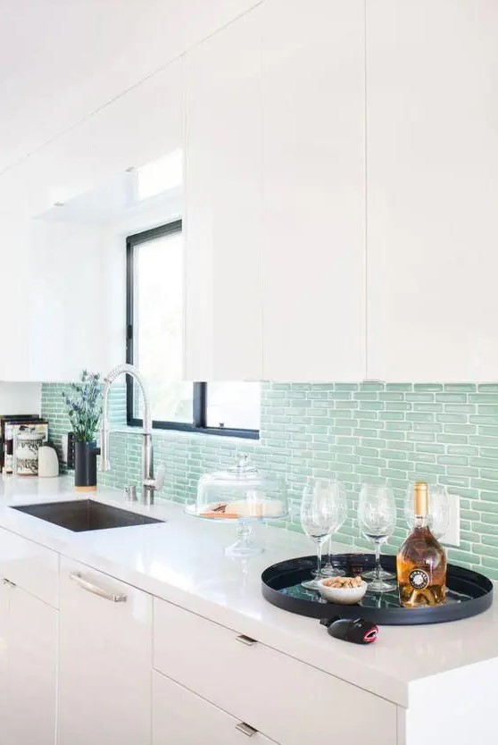 a modern white kitchen with sleek cabinetry, a mint green tile backsplash, black touches and white stone countertops