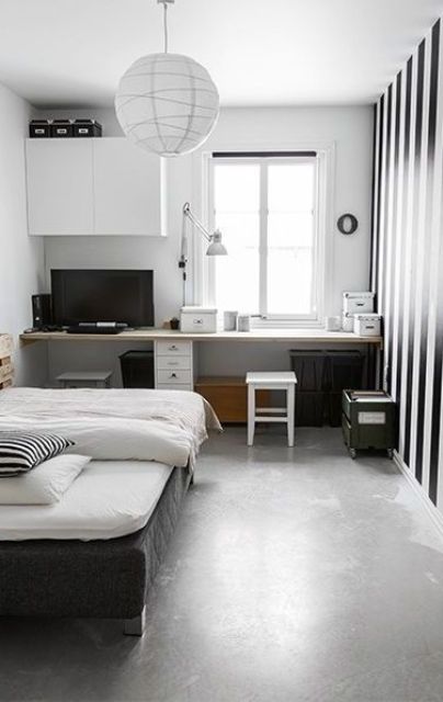 a monochromatic bedroom with a working space by the window, a TV, a striped accent wall, a black bed with neutral bedding