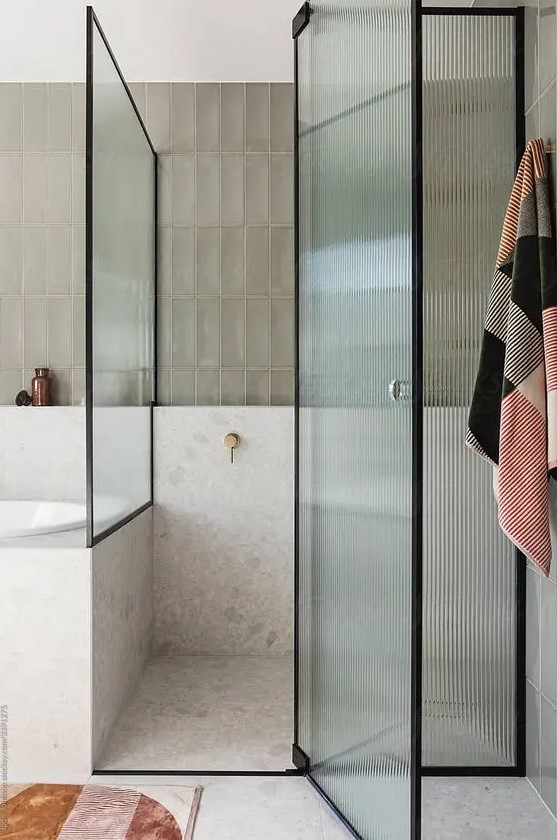 a neutral bathroom with a shower space enclosed in glass, with fluted glass doors and black framing is a chic and lovely idea