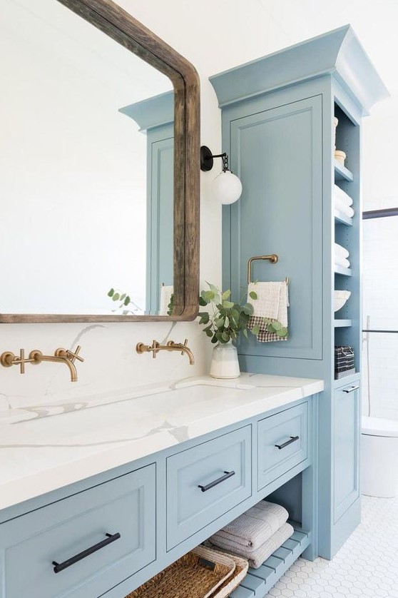 a neutral bathroom with light blue furniture, white marble, white hex tiles and a large mirror in a wooden frame