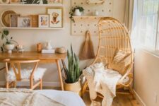 a neutral boho bedroom with a neutral bed with boho bedding, a stained desk and a chair, an egg-shaped chair and artwork and greenery