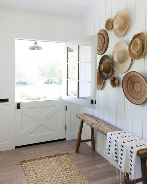 a neutral boho entryway with a gallery wall of hats and woven dishes, a white Dutch door, a stained bench and printed textiles
