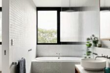 a neutral contemporary bathroom with grey granite tiles, a bathtub and a shower space with a fluted glass space divider, a large window