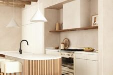 a neutral kitchen with flat panel cabinets and a large hood, a fluted and curved kitchen island and pendant lamps