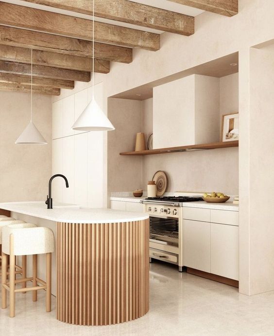 a neutral kitchen with flat panel cabinets and a large hood, a fluted and curved kitchen island and pendant lamps