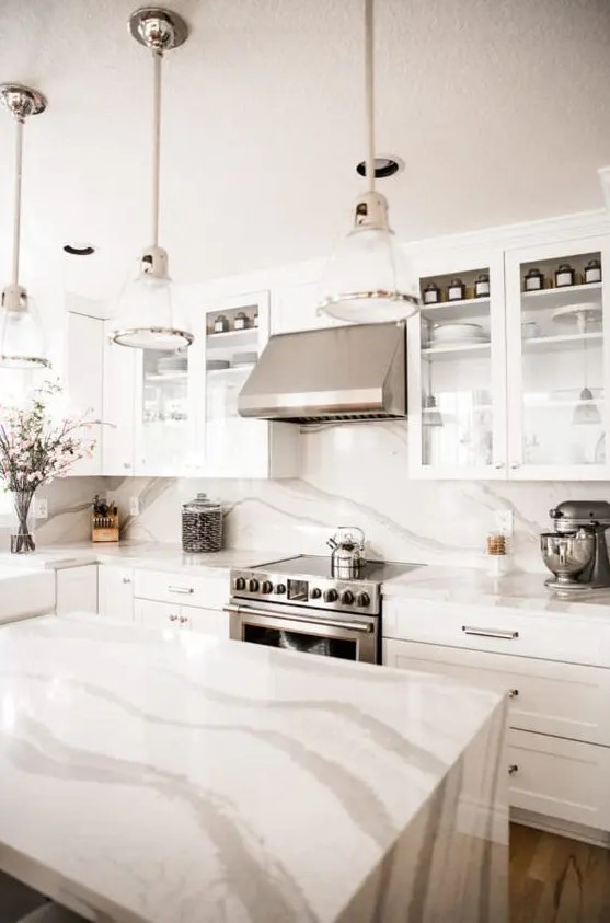 a neutral kitchen with shaker cabinets and glass ones, a white quartz backsplash and matching countertops, elegant lamps