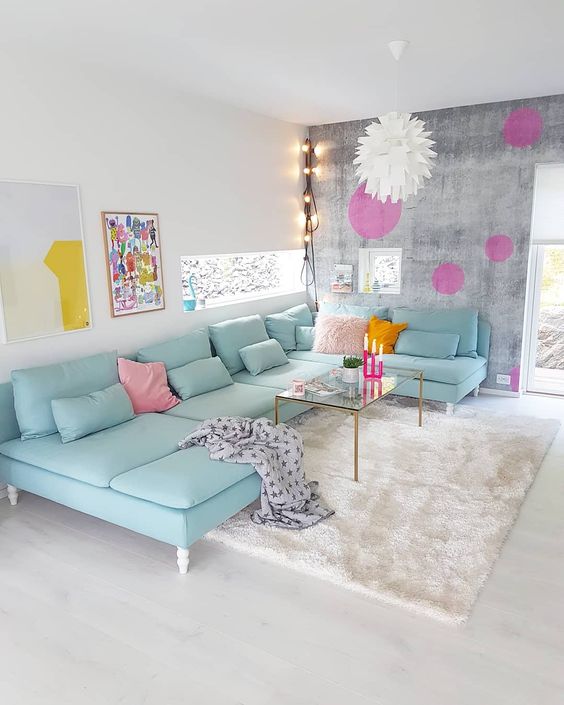 a neutral living room with a brushed accent wall, a mint blue sectional sofa with pillows, bold artwork and decorations