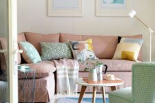 a neutral living room with a dusty pink sofa and printed pillows, a green chair, a pink and blue geo rug and a small coffee table