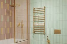 a pastel bathroom with a green and mauve skinny tile wall, a mauve floor and a toilet, brass fixtures