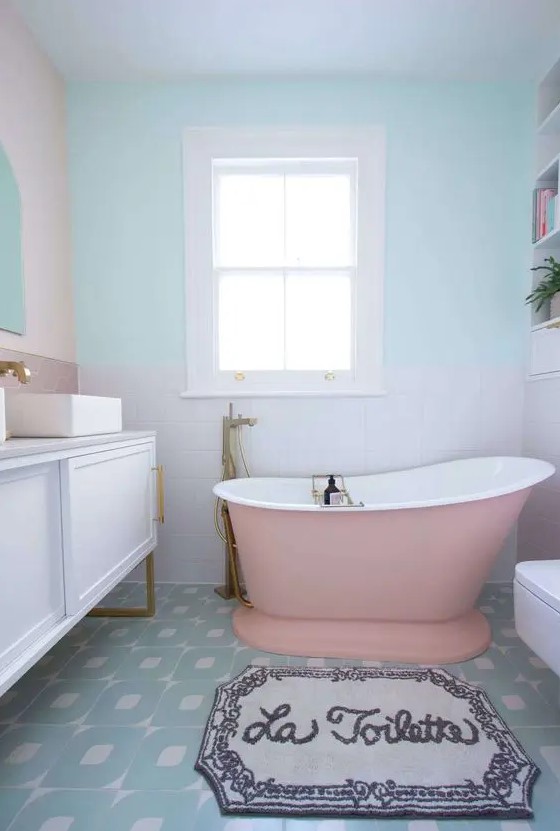 a pastel bathroom with blush and pastel blue walls, white square and pink hexagon tiles, a pink bathtub and a white vanity