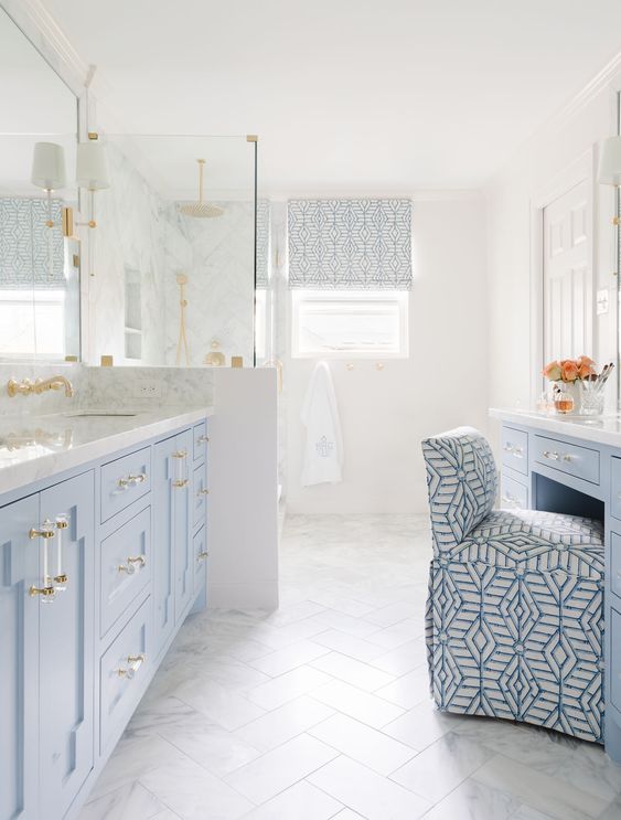 a pastel blue and white bathroom with a herringbone tile floor, a dusty blue vanity and a makeup table, a shower space and mirrors
