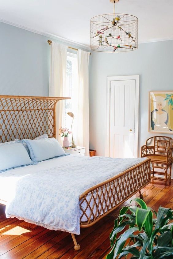a pastel blue bedroom with a rattan bed and chair, blue bedding, a whimsical cage chandelier and a potted plant