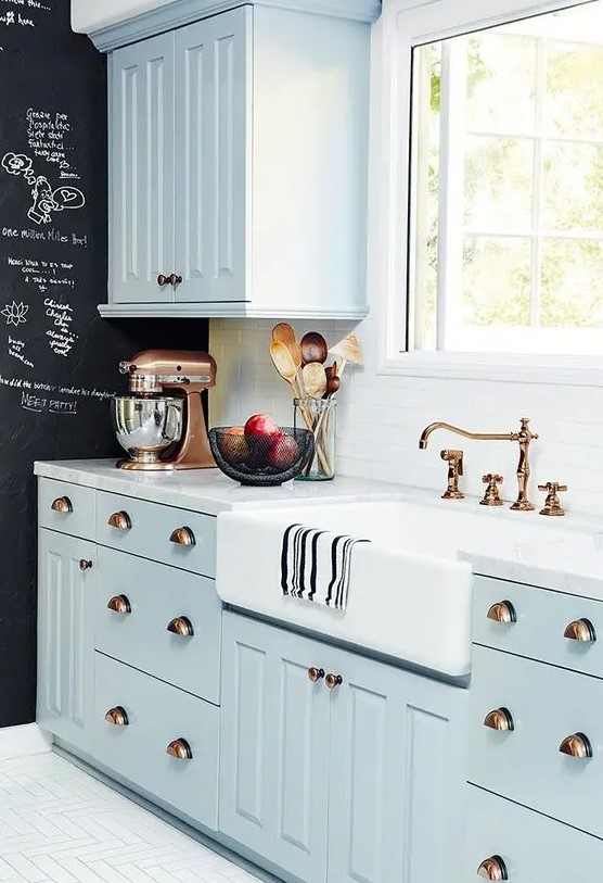 a pastel blue famrhouse kitchen with shaker cabinetry, a white stone countertop and a white tile backsplash plus a chalkboard wall