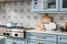 a pastel blue famrhouse kitchen with shaker cabinets, white granite countertops and a bold printed tile backsplash is wow