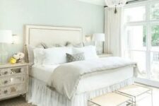 a pastel glam bedroom with an upholstered bed, a crystal chandelier, mirror nightstands and elegant stools