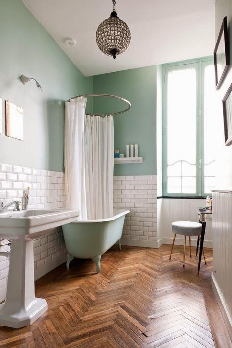 a pastel green bathroom with a parquet floor, a white subway tile backsplash, a green clawfoot tub and a cool pendant lamp