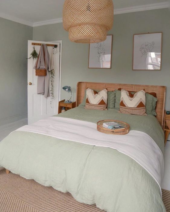 a pastel green bedroom with a rattan bed and nightstands, pastel green bedding, artwork and a woven pendant lamp