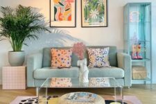 a pastel living room with a mint blue sofa, a mint blue glass cabinet, a pastel printed rug, a pink stool and printed pillows