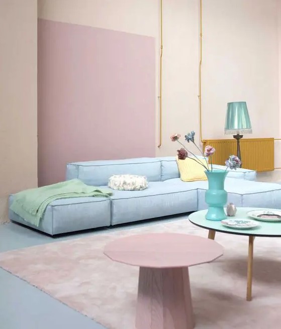 a pastel living room with blush walls, a pink accent, a pastel blue sofa, pastel side tables and a blue lamp