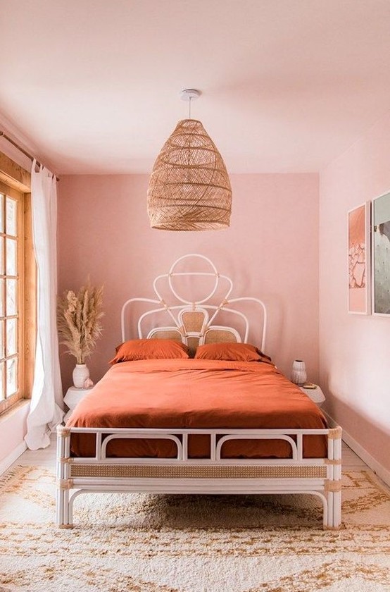 a pastel pink boho bedroom with a catchy white bed, rust bedding, a gallery wall, a boho rug and a large pendant lamp