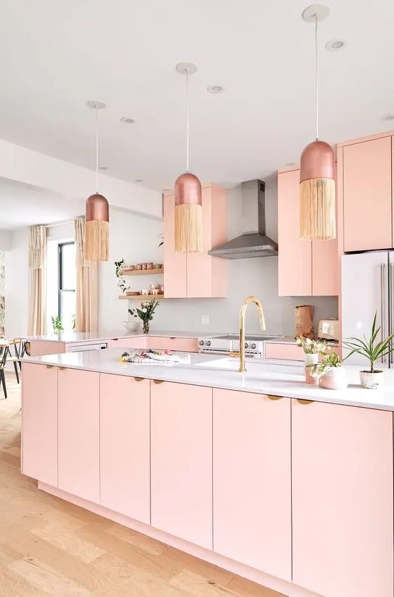 a pastel pink kitchen with plain cabinets, a large kitchen island, a white backsplash and coutnertops, pendant lamps with fringe