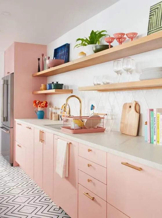 a pastel pink kitchen with plywood cabinetry, a white stone countertops, a white tile backsplash, gold handles