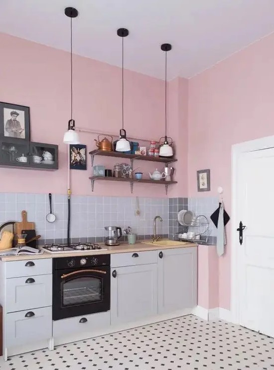 a pink kitchen with grey lower cabinets, butcherblock countertops, a grey tile backsplash, pendant lamps and a printed tile floor