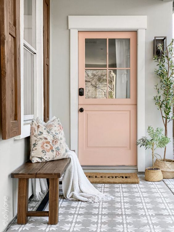 a pretty front porch with a printed tile floor, a stained bench with pillows, a salmon pink Dutch door, potted plants and a rug