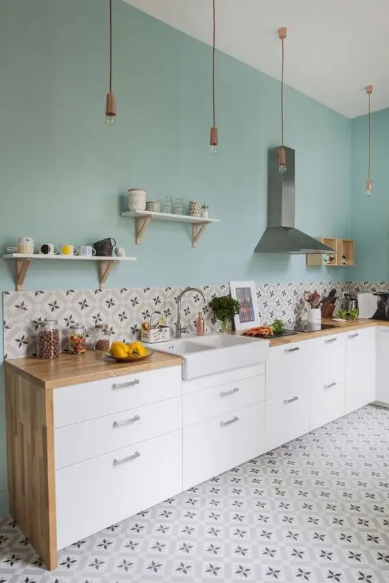 https://i.shelterness.com/2023/02/a-pretty-mint-blue-kitchen-with-sleek-white-cabinets-butcherblock-countertops-bold-printed-tiles-on-the-floor-and-backsplash-pendant-bulbs.jpg