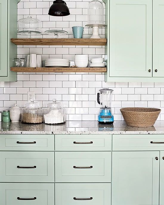 a pretty mint green farmhouse kitchen with shaker cabinets, open shelves, a white subway tile backsplash and neutral granite countertops
