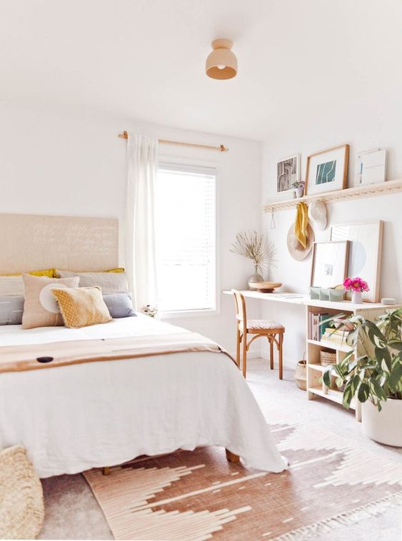 a pretty neutral boho bedroom with a small working nook in the corner, with a desk, a shelf and a chair, a bed with printed bedding and a rug