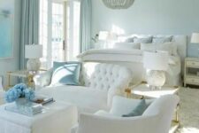 a refined pastel blue bedroom with white furniture, a white bed and bedding, blue curtains and a chic chandelier