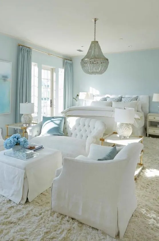 a refined pastel blue bedroom with white furniture, a white bed and bedding, blue curtains and a chic chandelier