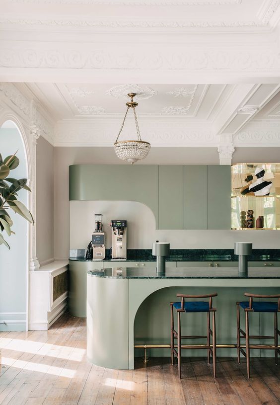 a refined sage green kitchen with a curved upper cabinet and a cutout curved kitchen island, tall blue stools and a chic chandelier