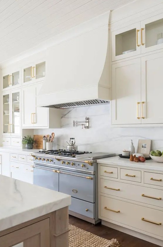 a refined vintage creamy kitchen with shaker cabinets, a white quartz backsplash and countertops, brass and gold fixtures