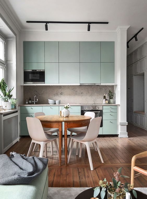 a sage green Scandinavian kitchen with flat panel cabinets, a round table, neutral chairs, a stone backsplash and black lamps