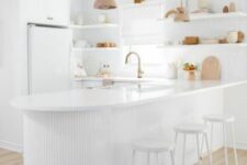 a serene white kitchen with a large curved and fluted kitchen island, open shelves, wooden pendant lamps and white stools