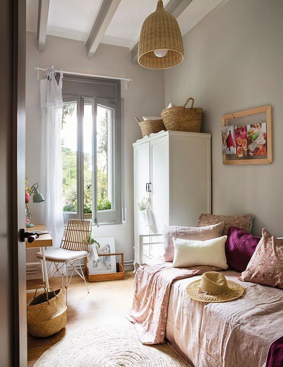 a small modern rustic guest bedroom with a stained desk and a chair, a bed with pastel bedding, a white wardrobe and baskets