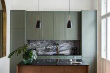 a small vintage-inspired kitchen with green shaker cabinets, a stained kitchen island, black countertops and a backsplash, black pendant lamps