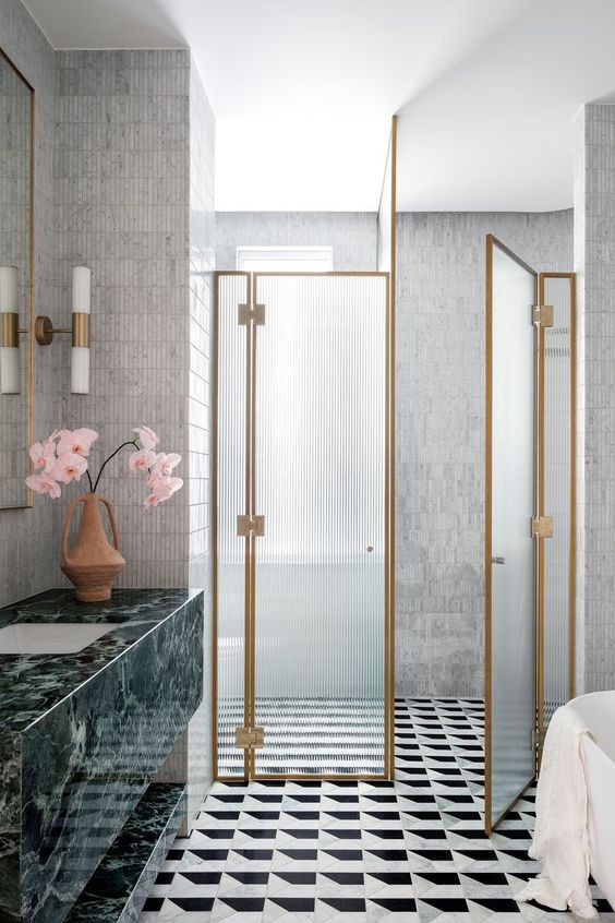 a sophisticated bathroom with a printed tile floor, a fluted glass shower screen, a green marble vanity and skinny tiles on the walls